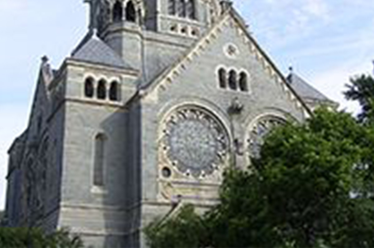 Fassade einer neoromanischen Steinkirche mit zwei großen Fensterrosen.